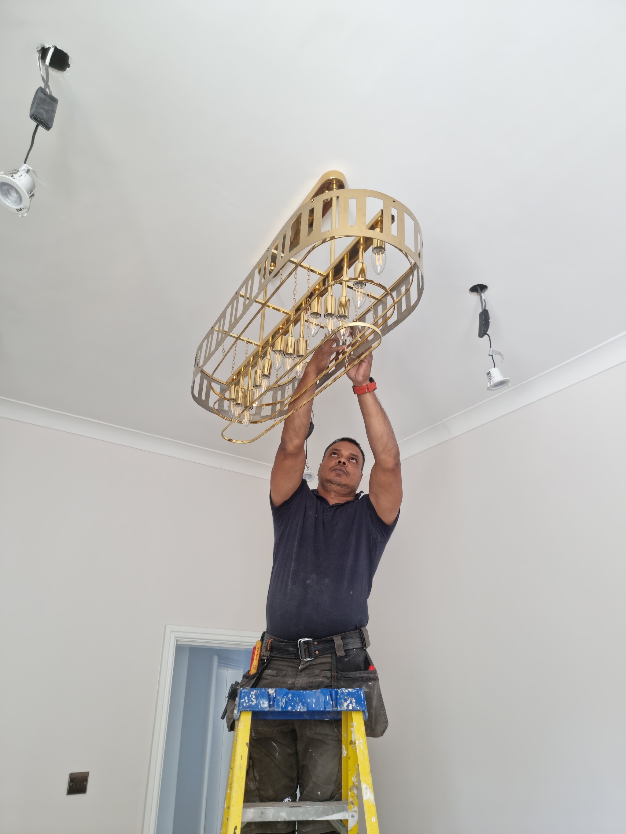 Naz on a stepladder fitting a brass chandelier to a newly painted ceiling