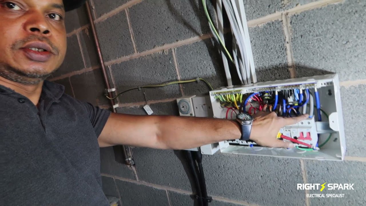 Naz reaching into a consumer unit mounted on a blockwork wall