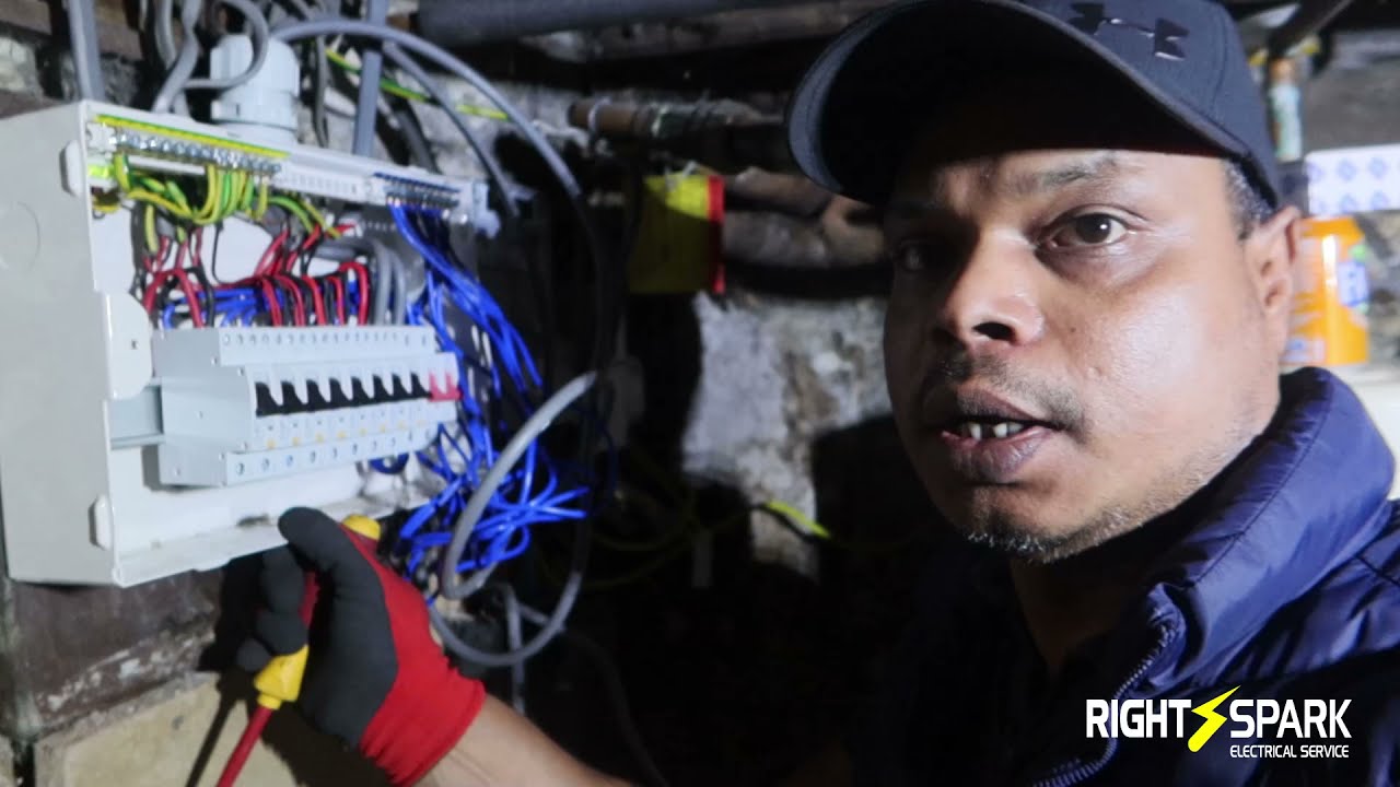 Naz beside a newly fitted consumer unit in a cellar, holding a voltage tester