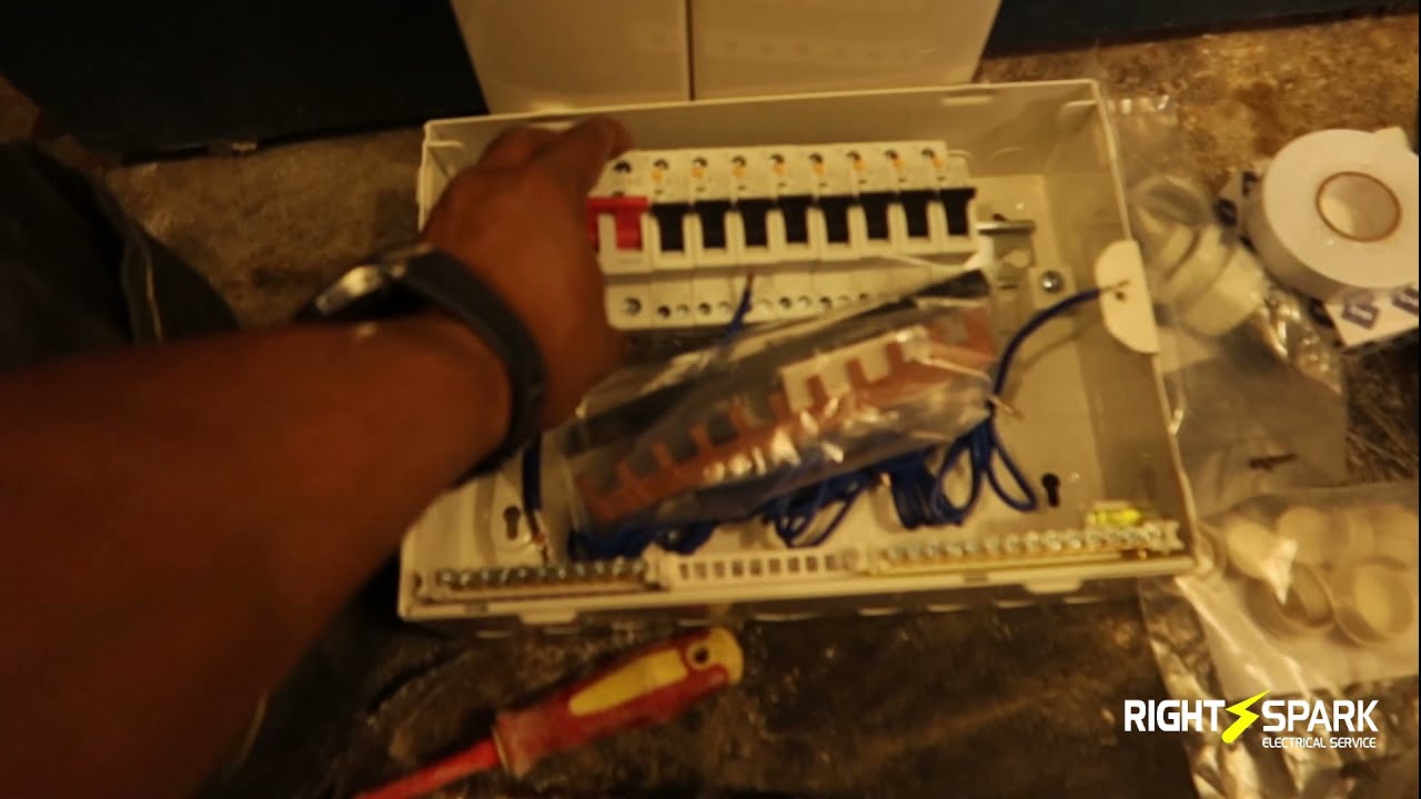 A hand resting on an open consumer unit with a row of breakers