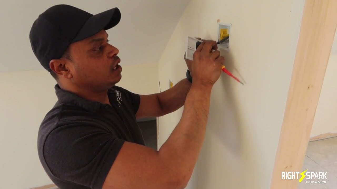 Naz in a Right Spark polo shirt fixing a switch plate to a newly plastered wall