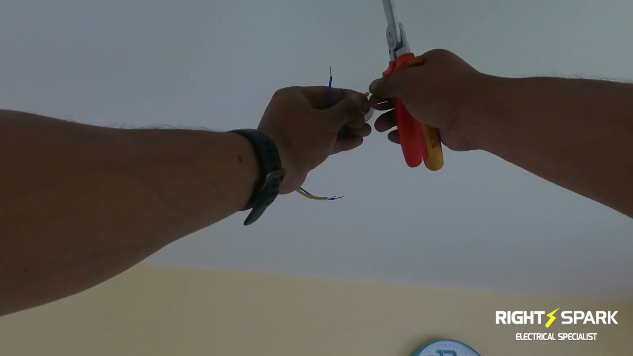 Hands stripping a cable with red cutters just below a ceiling